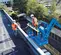 Front angled view of two workers in safety gear operating a blue Genie boom lift on a rooftop parking lot.
