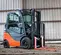 Front angled view of orange and grey Toyota warehouse forklift with a mast, orange forks and enclosed cabin in a warehouse.