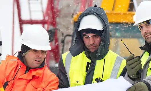 Travailleurs portant des gilets de sécurité et des casques de sécurité sur un chantier de construction en hiver