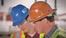 Two men on a construction site wearing hard hats, safety vests and safety glasses.