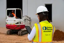 femme sur un chantier tenant un iPad près d’une chargeuse à direction à glissement