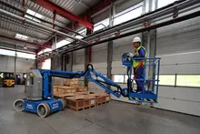 Travailleur sur une nacelle élévatrice électrique à l’intérieur d’un entrepôt