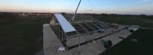Installation d’un panneau de toiture sur une grande structure temporaire en toile à l’aide d’une grue au crépuscule dans un champ ouvert